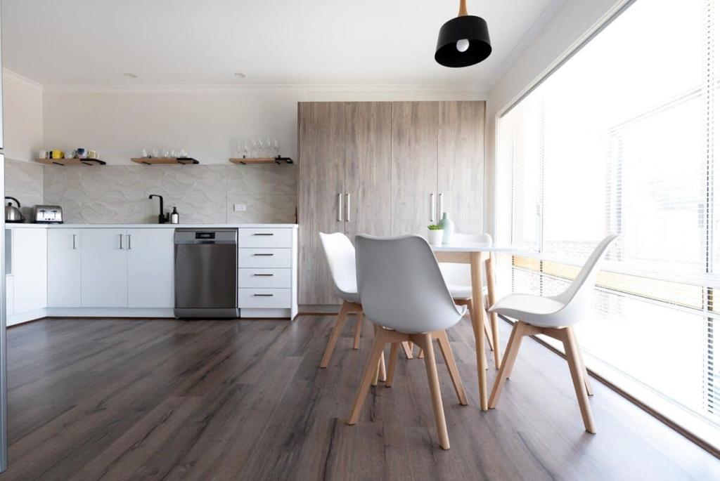 Una cocina con gabinetes blancos y una mesa y sillas. en Cosy & Sweet: Near the City WiFi =& Parking, en Kings Park