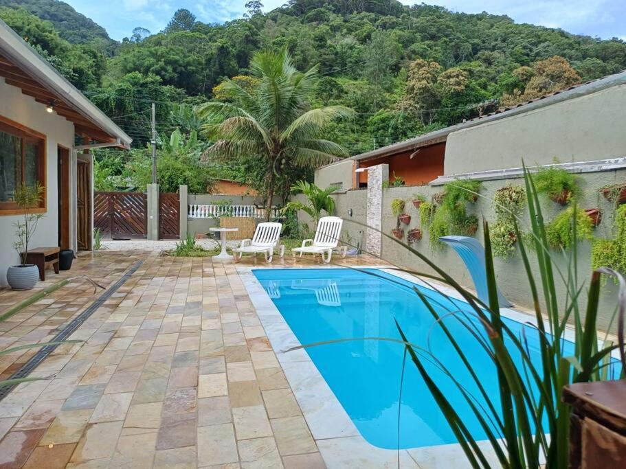 a swimming pool in a yard with two chairs and a house at Casa Luz do Sol Ubatuba in Ubatuba