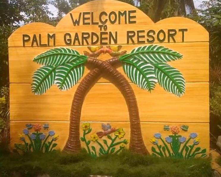 a sign for a palm garden resort with a palm tree at Palm Garden Resort in Carles