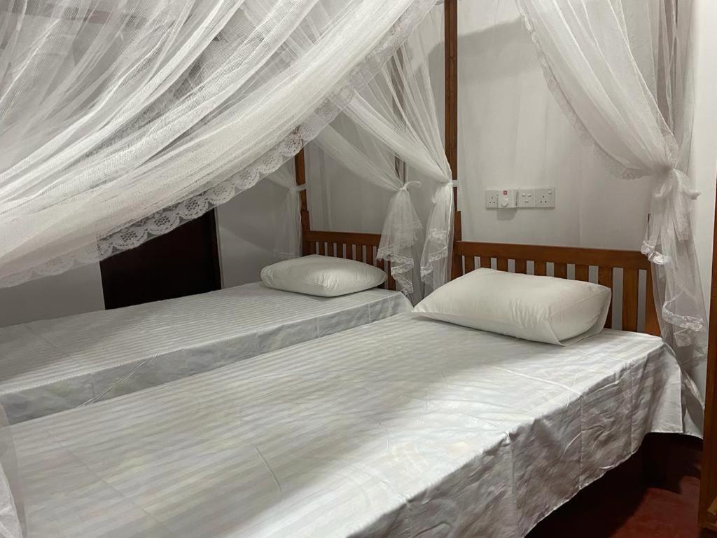 two beds in a bedroom with white drapes at Pacifia Villa in Bentota