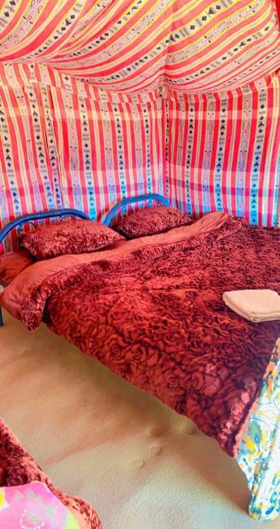a bed with a red comforter on top of it at Desert heart camp in Al Wāşil