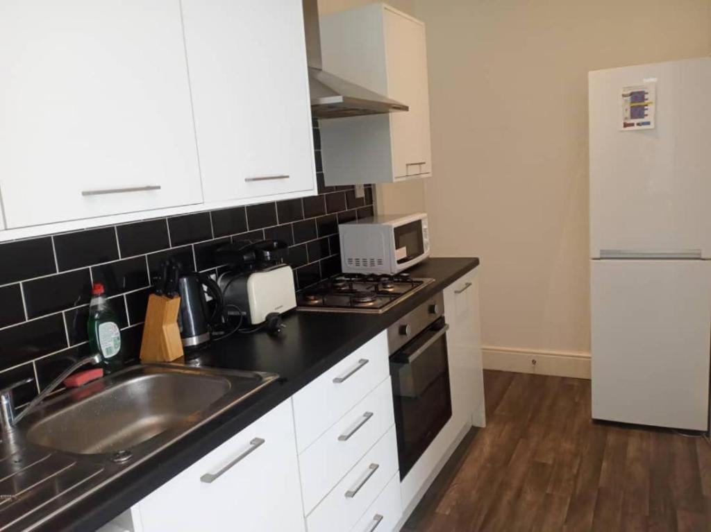 cocina con armarios blancos, fregadero y nevera en Double bed (R2) close to Burnley city centre, en Burnley