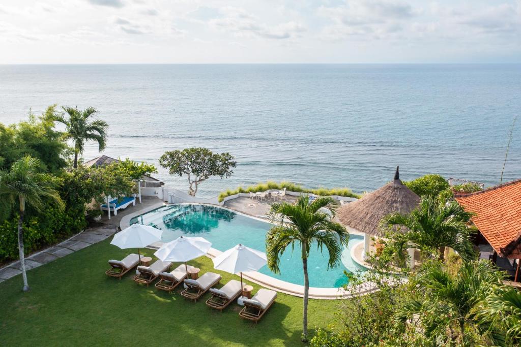 an infinity pool with chairs and umbrellas and the ocean at Villa Nirvana Biru Bingin Beach in Uluwatu