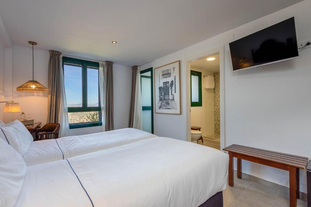 a bedroom with a large white bed and a television at Hotel Tugasa Arco de la Villa in Zahara de la Sierra