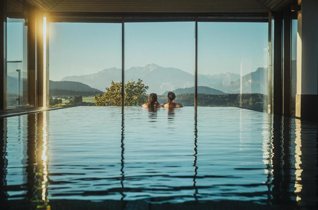 dos niños nadando en una piscina con montañas en el fondo en Romantik Spa Hotel Elixhauser Wirt en Elixhausen