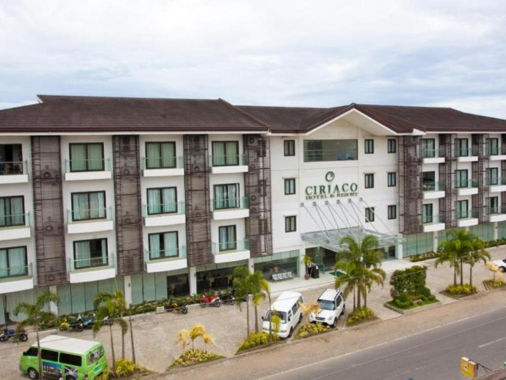 ein großes weißes Gebäude mit Autos auf einem Parkplatz in der Unterkunft Ciriaco Hotel in Calbayog