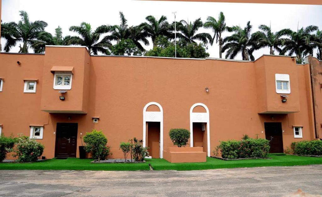 a orange building with palm trees in the background at AJ HOMES in Benin City