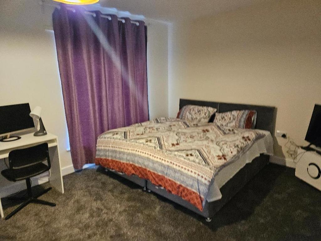 a bedroom with a bed with purple curtains and a desk at 1 Bedroom en suite ASHLAND, Milton keynes in Fenny Stratford