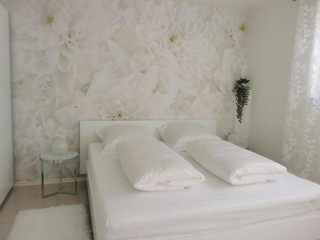 ein weißes Bett mit zwei Kissen und eine Wand mit Blumen in der Unterkunft Ferienwohnung Edelweiß in Rust