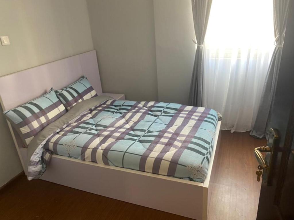 a bedroom with a bed with a plaid blanket and a window at Very secure apartment Bole Addis Enyi Real Estate in Addis Ababa