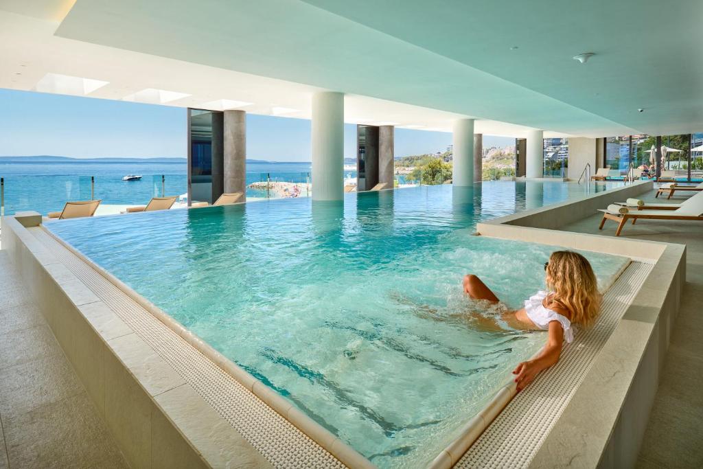 una niñita sentada en una piscina infinita en Amphora Hotel, en Split