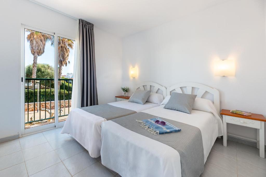 two beds in a hotel room with a balcony at Vibra Caleta Playa Apartmentos-3SUP in Sa Caleta