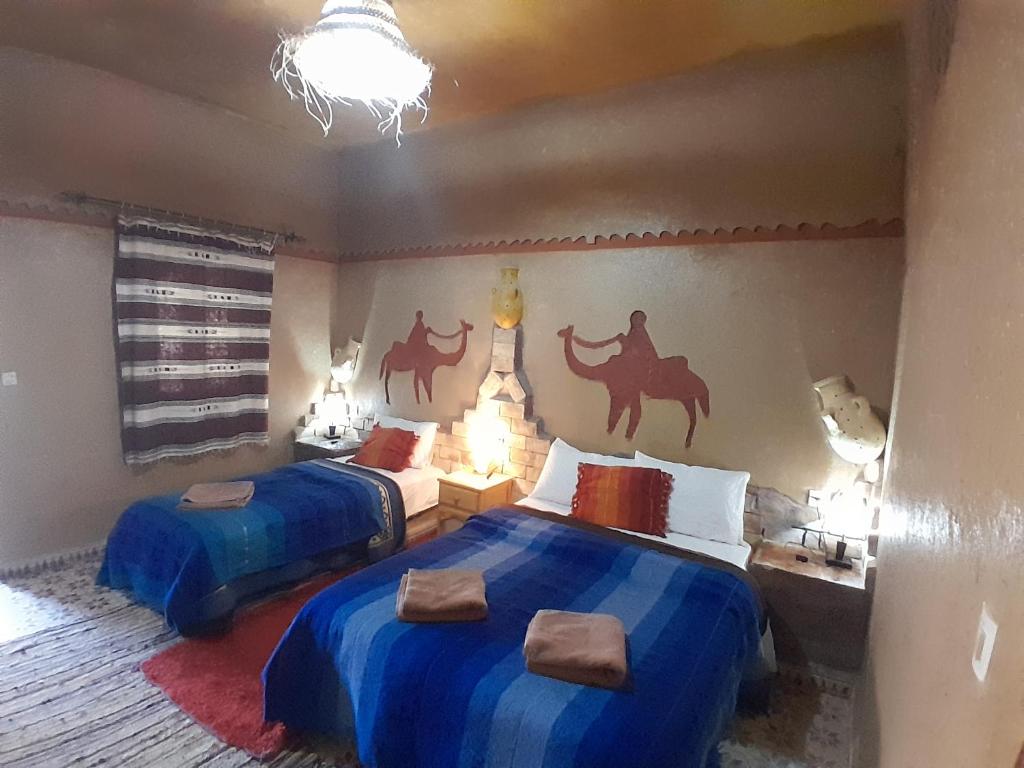 - une chambre avec 2 lits avec des draps bleus et des peintures murales à dos de chameau dans l'établissement Auberge Camping La Liberté, à Merzouga