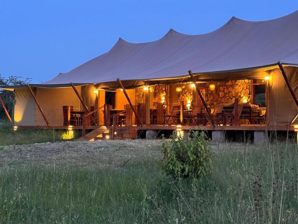 a safari tent with tables and chairs in a field at Alama Camp Mara in Ololaimutiek