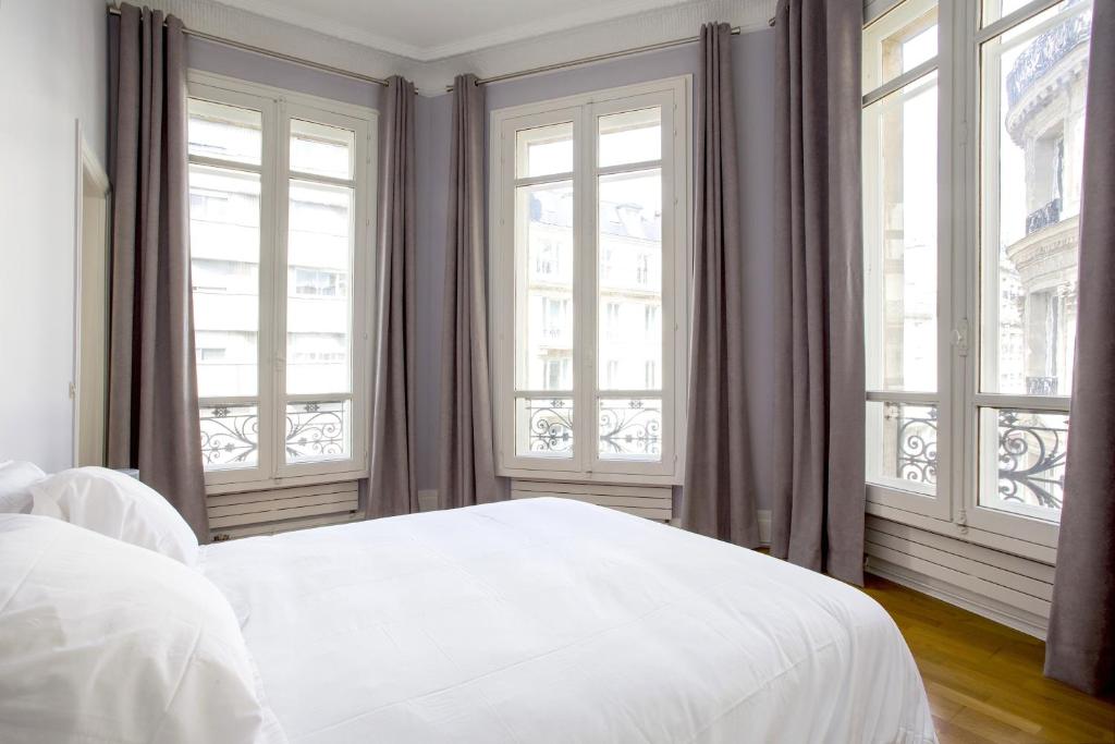 a white bed in a room with windows at Appartement Caumartin Lafayette in Paris