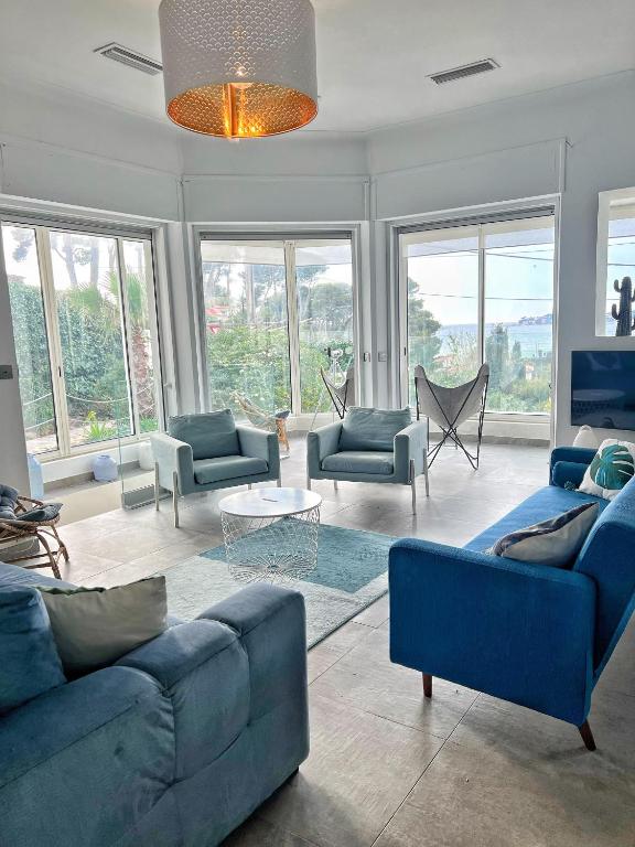 - un salon avec des canapés bleus, des chaises et des fenêtres dans l'établissement Villa avec piscine, Baie de Bandol, Accès plage, à Sanary-sur-Mer