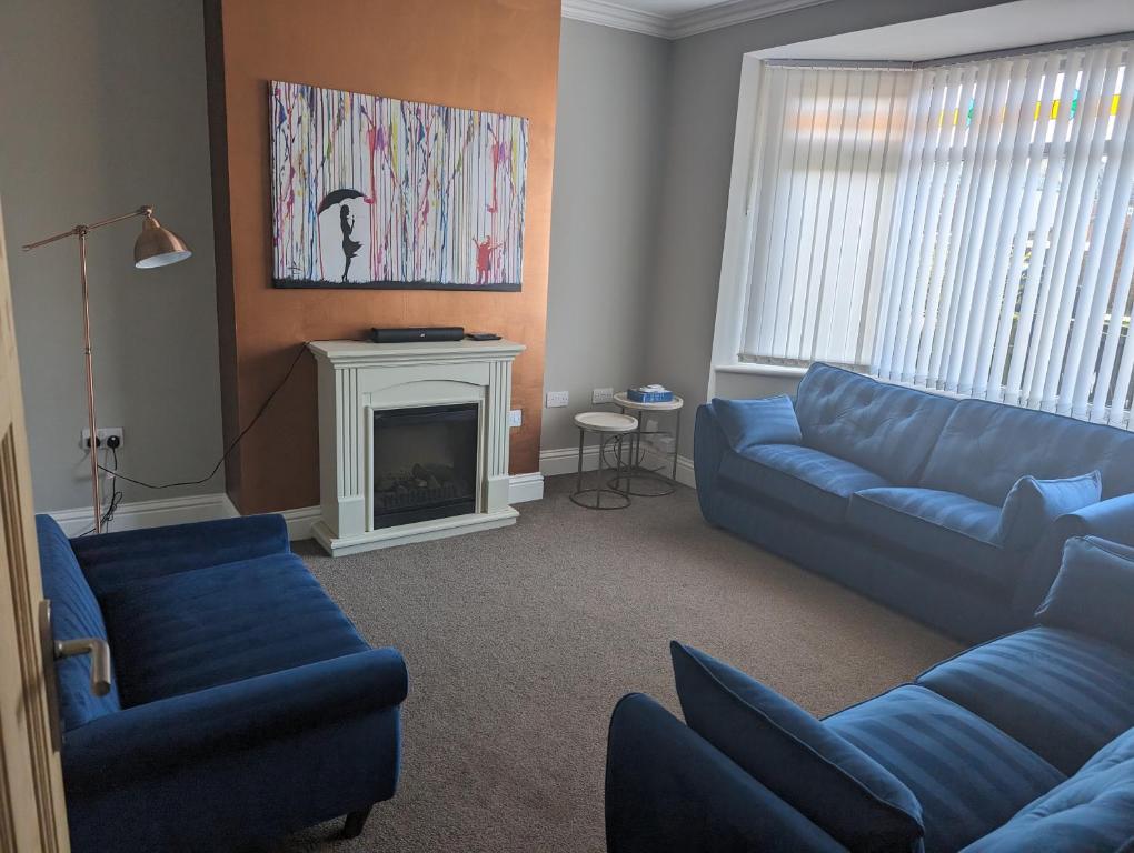 a living room with blue couches and a fireplace at 3 bed home, pool-hot tub & ev charger in Darlington