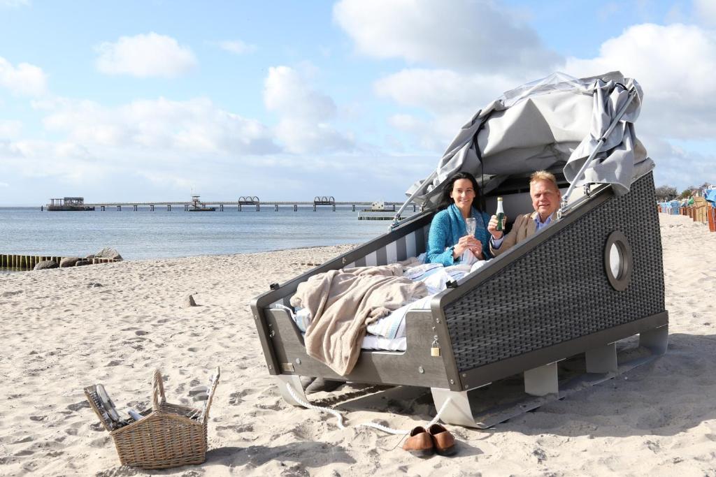 a man and woman sitting in a bed on the beach at Schlafstrandkorb Nr 2 in Kellenhusen