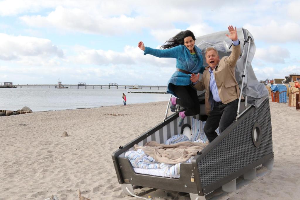 un homme et une femme sautant sur une remorque sur la plage dans l'établissement Schlafstrandkorb Nr 4, à Kellenhusen