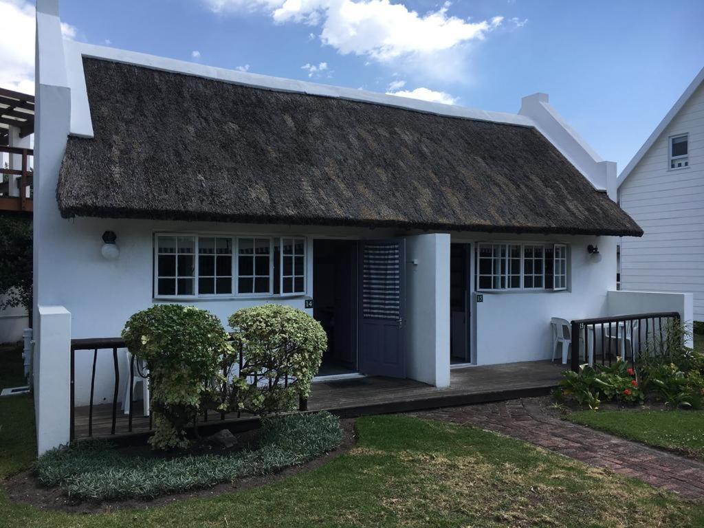 a white house with a thatched roof and a porch at Seals Backpackers in Cape St Francis