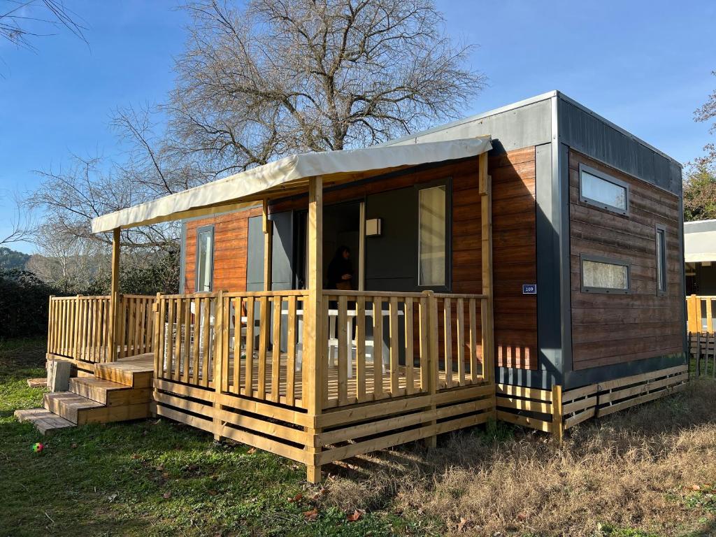 uma cabana de madeira com um alpendre na relva em MobilHome Comfort XL (37m2) : 2 Chambres (6 personnes) - 2 SDB - Clim centralisée - TV - Terrasse balcon em Cadenet