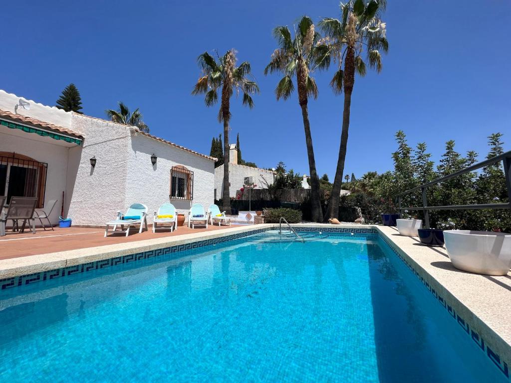 einen Pool mit Stühlen und ein Haus mit Palmen in der Unterkunft Cd-1383 Three Bedroom Villa With Pool in Viñuela