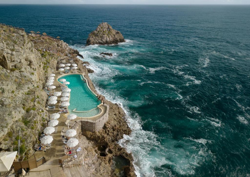 a swimming pool on a cliff next to the ocean at UNA HOTELS Capotaormina in Taormina