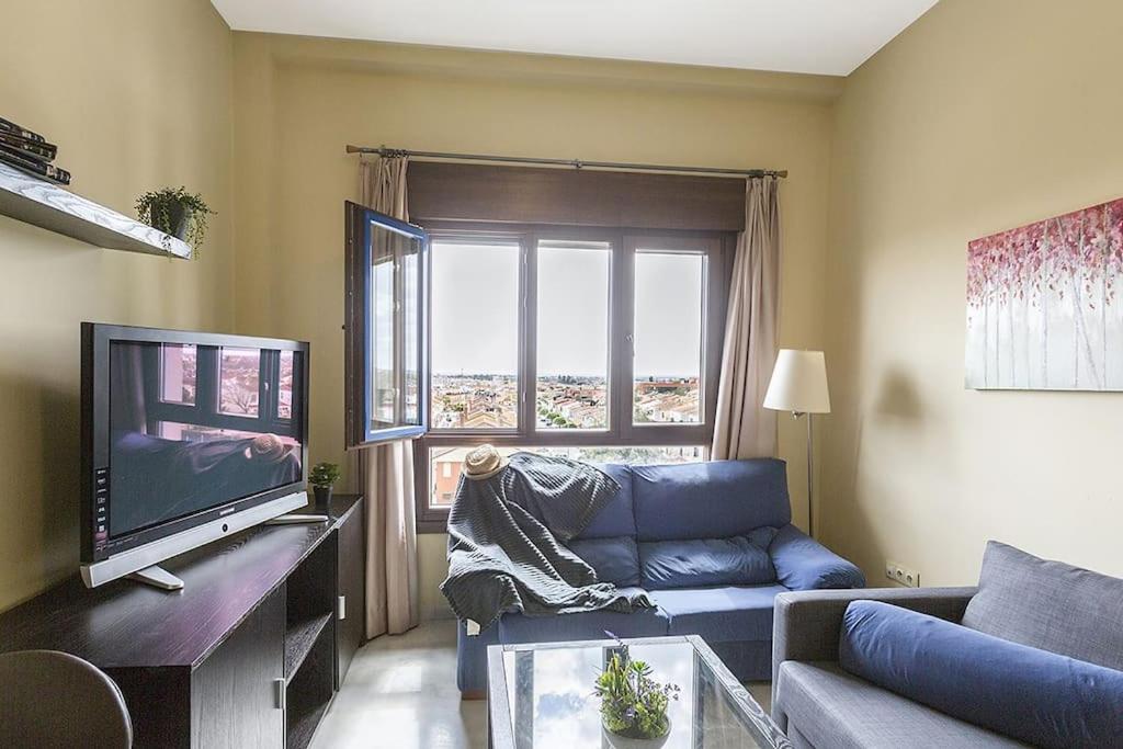a living room with a blue couch and a tv at Apartamento EL MIRADOR, recepción 24 h, piscina, wifi y parking interior in Bormujos