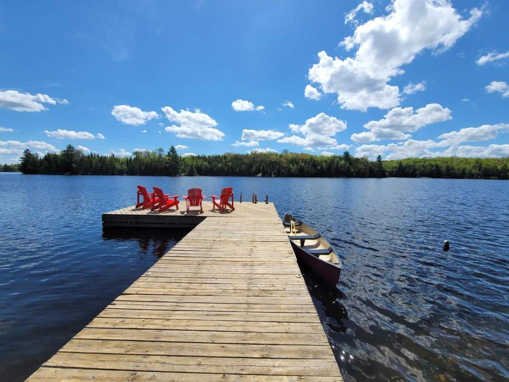 a dock with chairs and a boat on a lake at Firefly Hut - Cheerful 6-bedroom cottage with serene beauty in McDougall