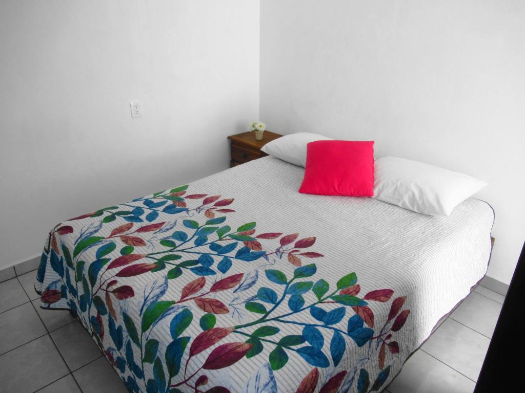 Una cama con una almohada roja encima. en Cocos, en Cancún