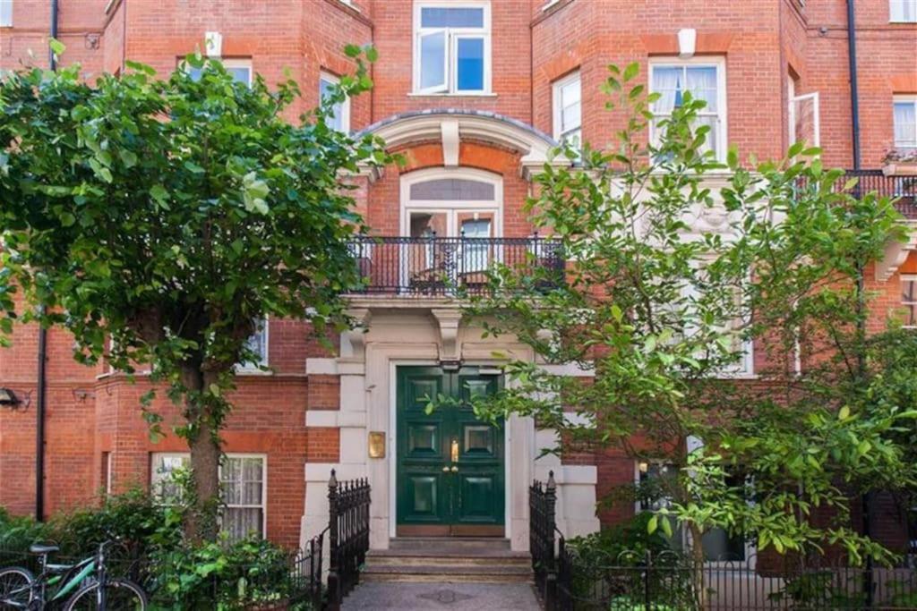 a green door on a brick building with trees at Spacious Flat in West Kensington in London