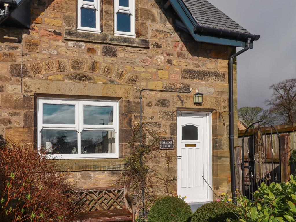 a stone house with a white door and windows at Jasmine Cottage in Alnwick