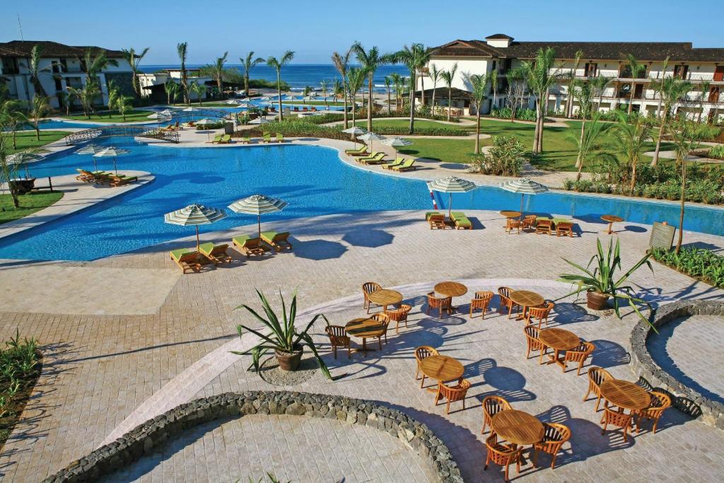 Oceanfront resort with freeform pools, palm-fringed lawns, sun loungers and shaded wooden dining tables at JW Marriott Guanacaste Beach Resort in Tamarindo