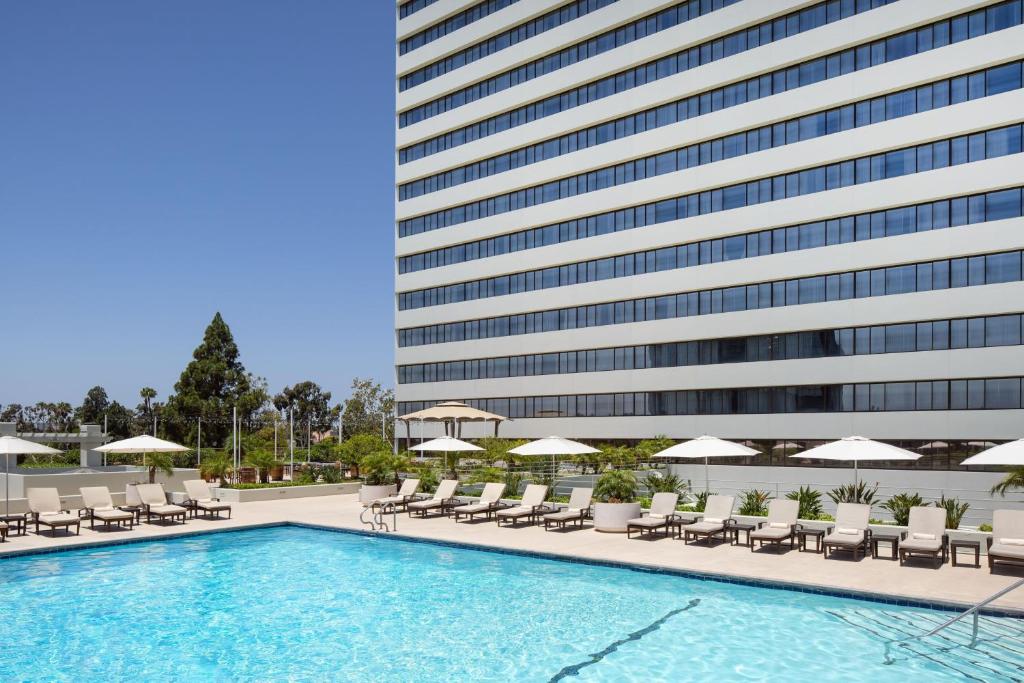 uma piscina com cadeiras e guarda-sóis ao lado de um edifício em The Westin South Coast Plaza, Costa Mesa em Costa Mesa