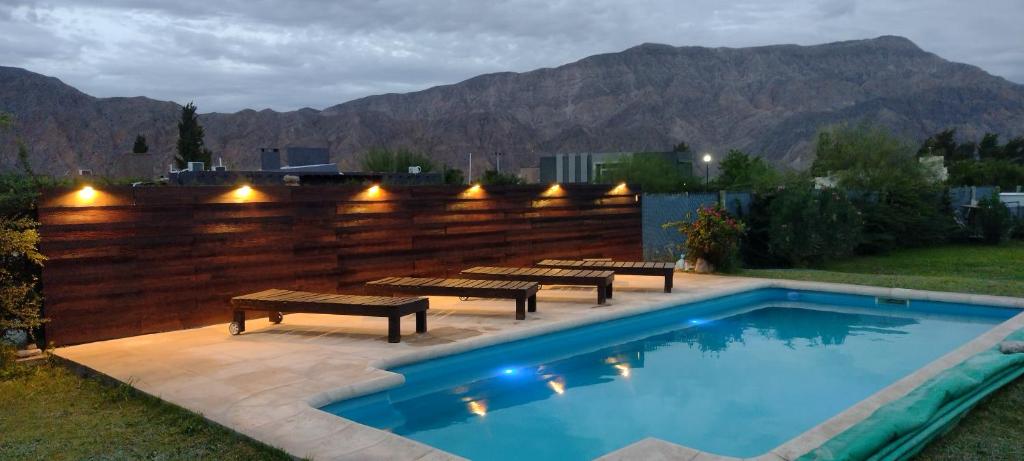 a swimming pool with benches and a fence with mountains at Sol de las Sierras Zonda PREVIAJE in Zonda
