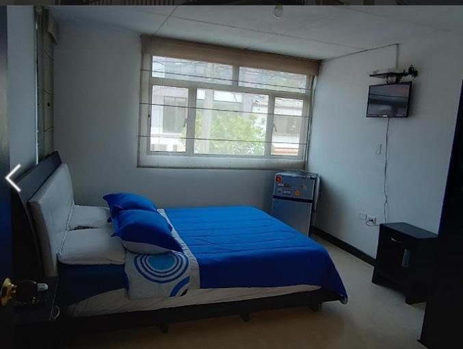 Schlafzimmer mit einem Bett mit blauer Bettwäsche und einem Fenster in der Unterkunft Casa de Huéspedes Santa María Hotel in Bogotá