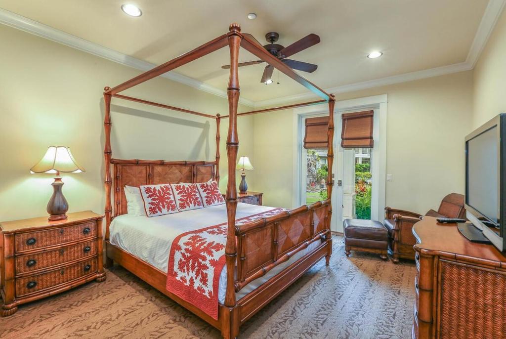 Un dormitorio con una cama con dosel y un televisor de pantalla plana. en Ground Floor Luxury Penthouse in Poipu Kai, en Koloa