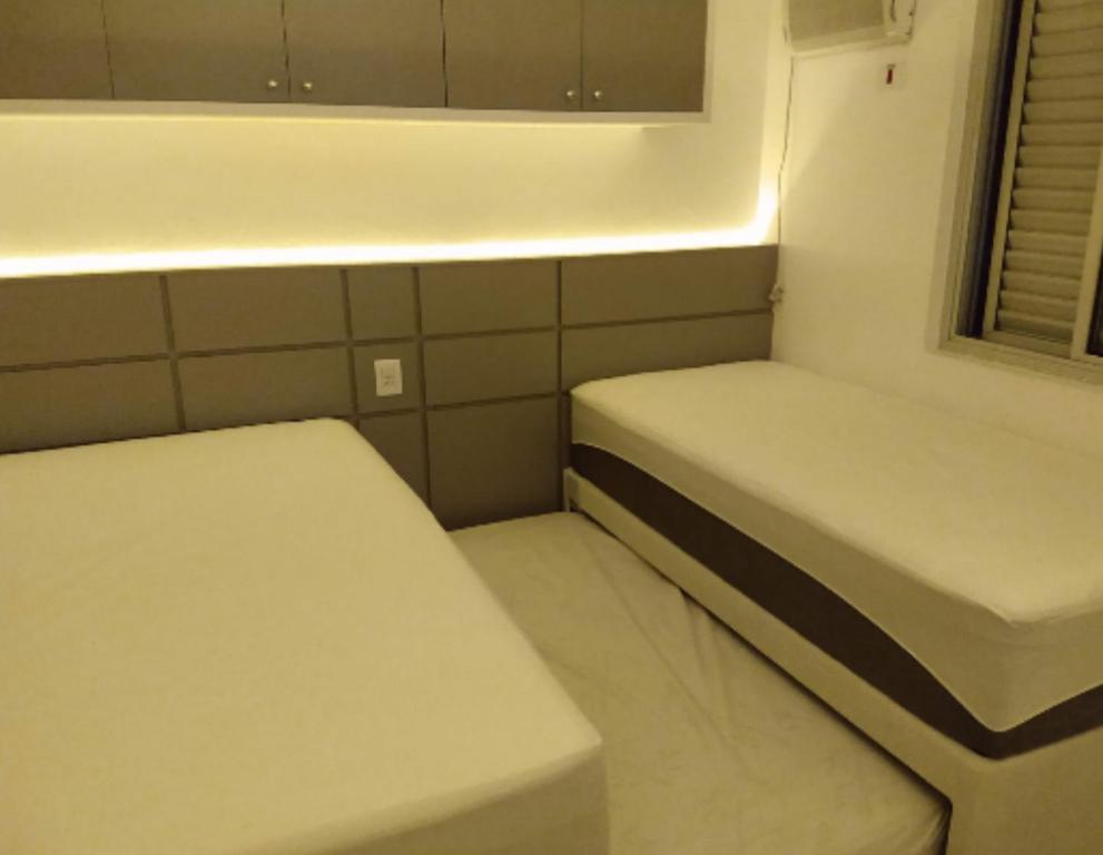 a small room with two beds and a window at Apt Guarujá Enseada lado praia FAN 1 dorm Tv Netflix Wi-Fi Ar até 5 pessoas in Guarujá