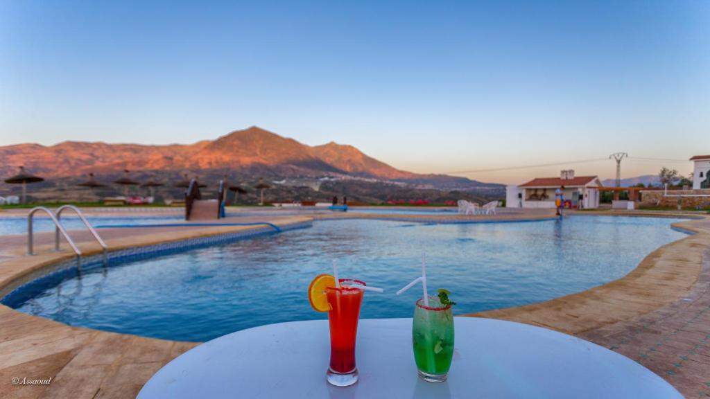 dos bebidas sentadas en una mesa junto a una piscina en Hotel El Cortijo & SPA, en Chefchaouen