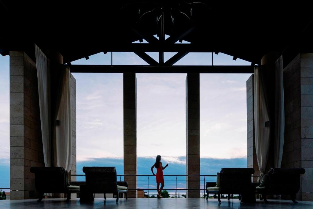 a woman in a red dress standing in front of a large window at The Romanos, a Luxury Collection Resort, Costa Navarino in Romanu