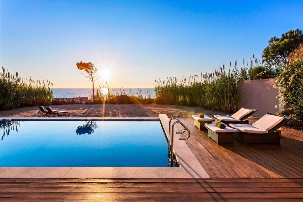 a swimming pool with chairs and the ocean in the background at The Romanos, a Luxury Collection Resort, Costa Navarino in Romanu