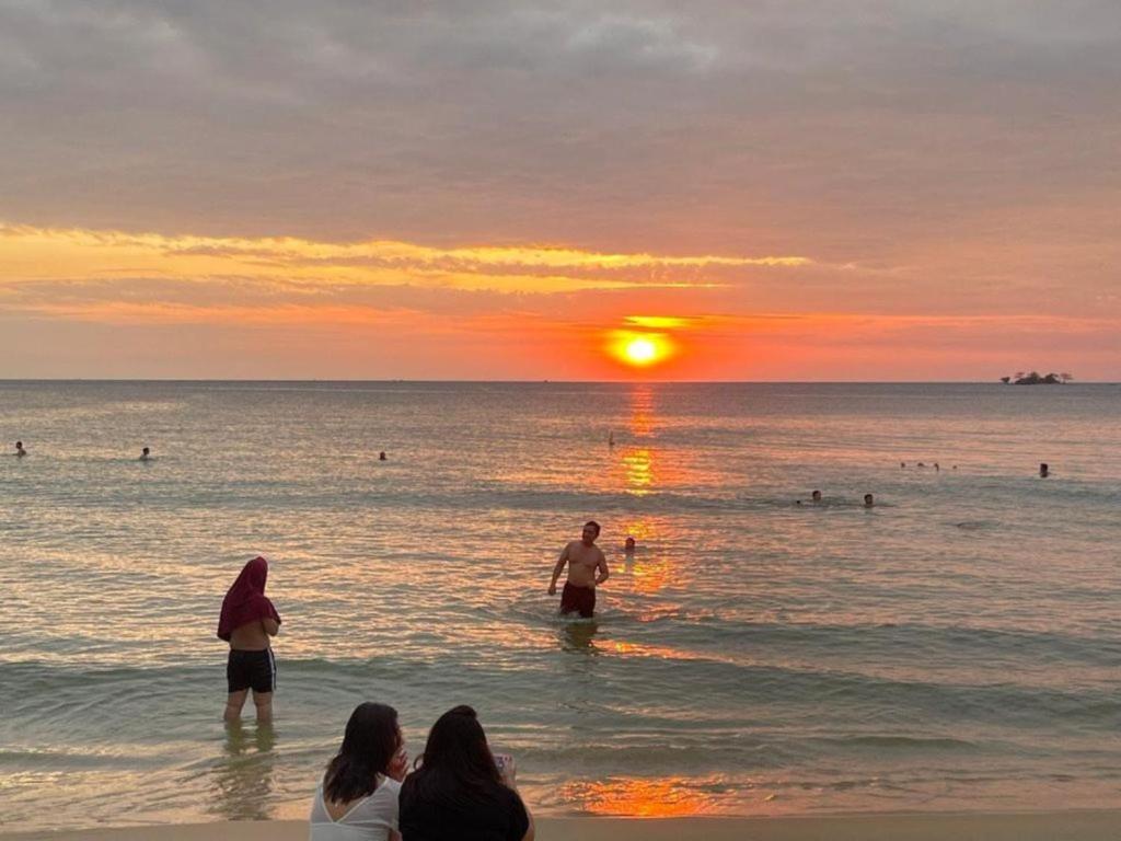 personas de pie en el agua en la playa al atardecer en Beach Hotel Grand World (La La Homestay), en Phu Quoc