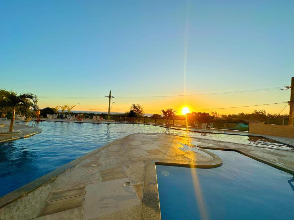 uma piscina com o pôr-do-sol ao fundo em Apartamento até 8 Pessoas Praia Grande - Le Bon Vivant em Arraial do Cabo