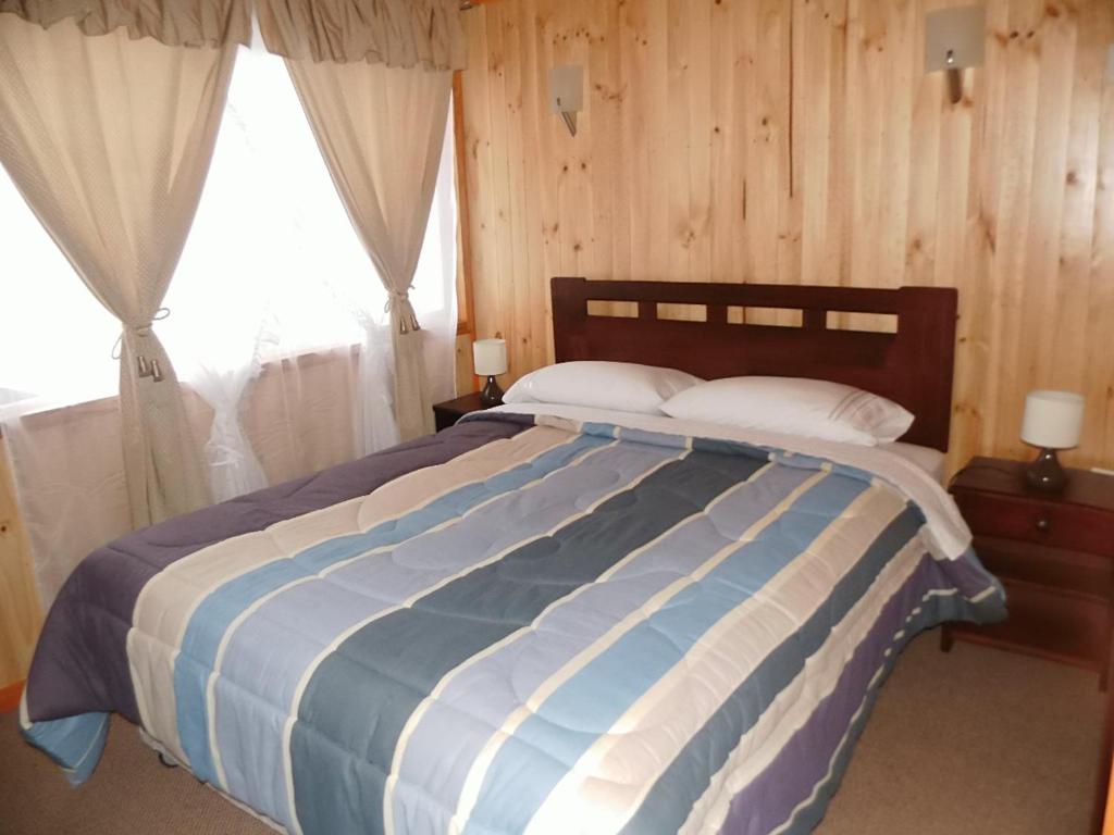 a bedroom with a bed with a blue and white striped blanket at Cabaña Choshuenco B & B in Choshuenco