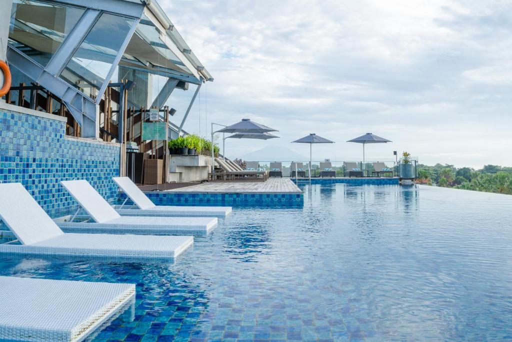 a swimming pool with white chairs and umbrellas at ARTOTEL Sanur Bali in Sanur