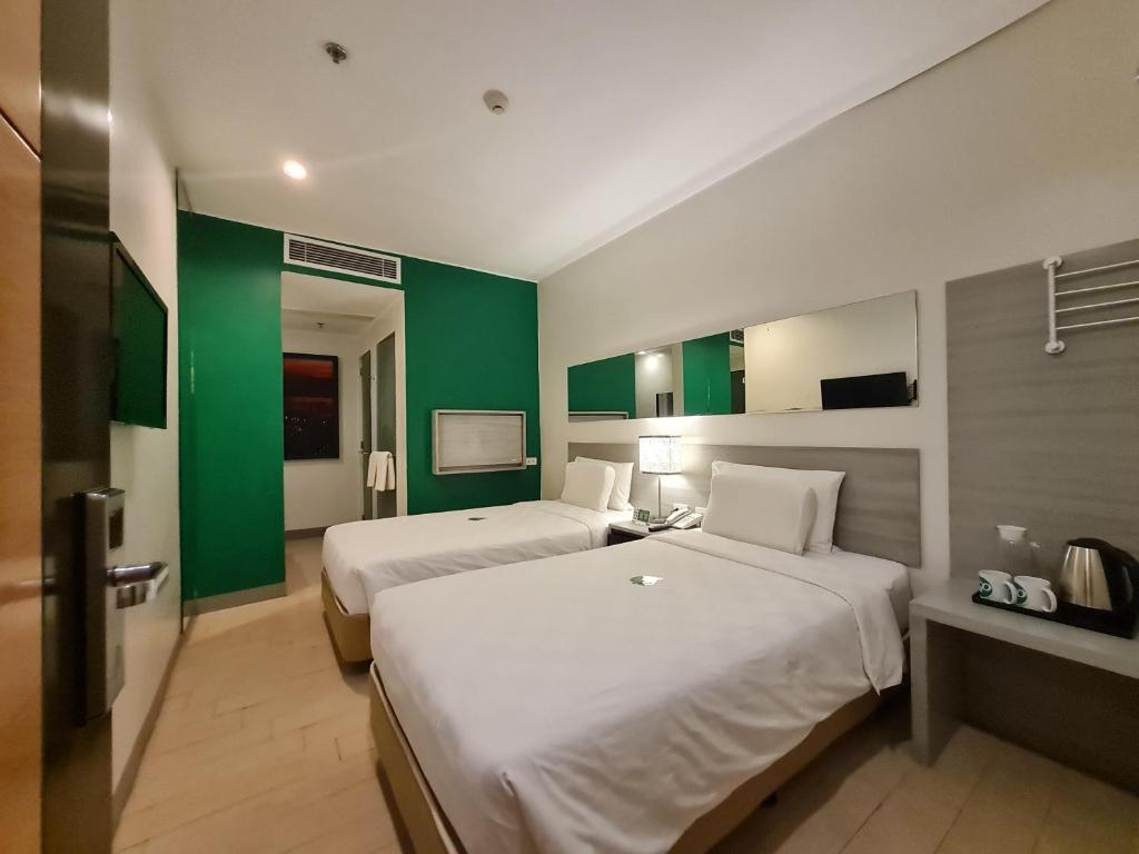 Go Hotels Otis - Manila في مانيلا: غرفة فندقية بسريرين وجدران خضراء