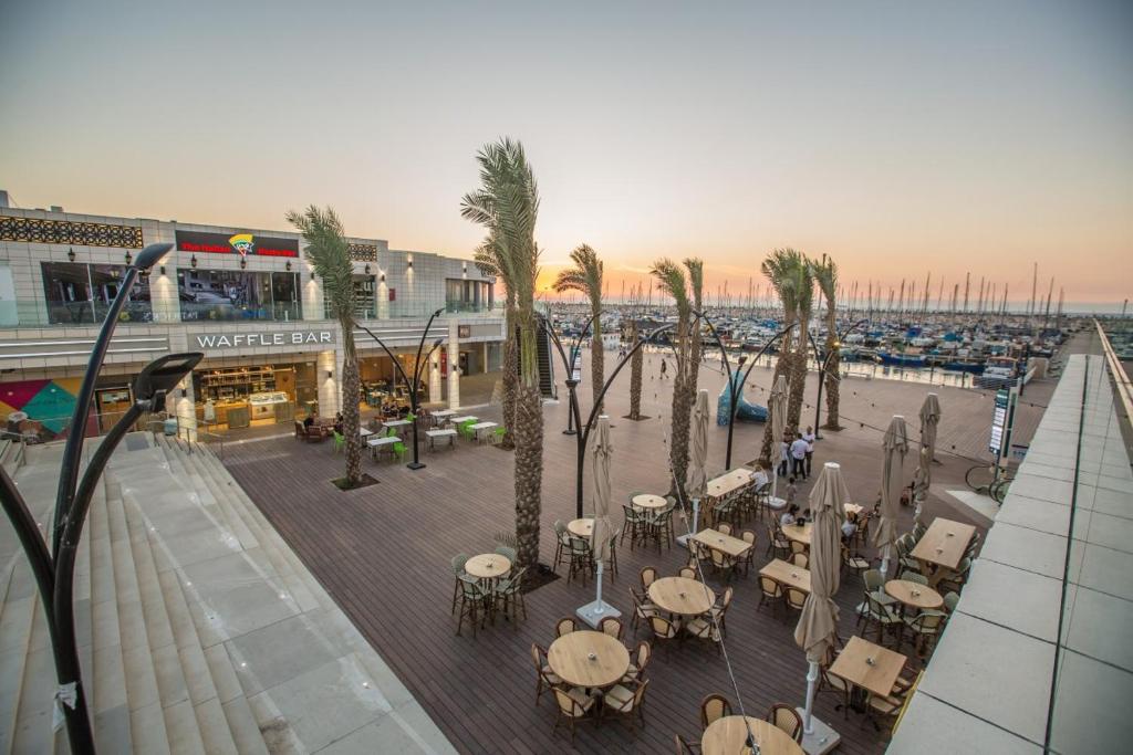 a street with tables and palm trees and a harbor at Sunset suite - step from the beach in Ashkelon