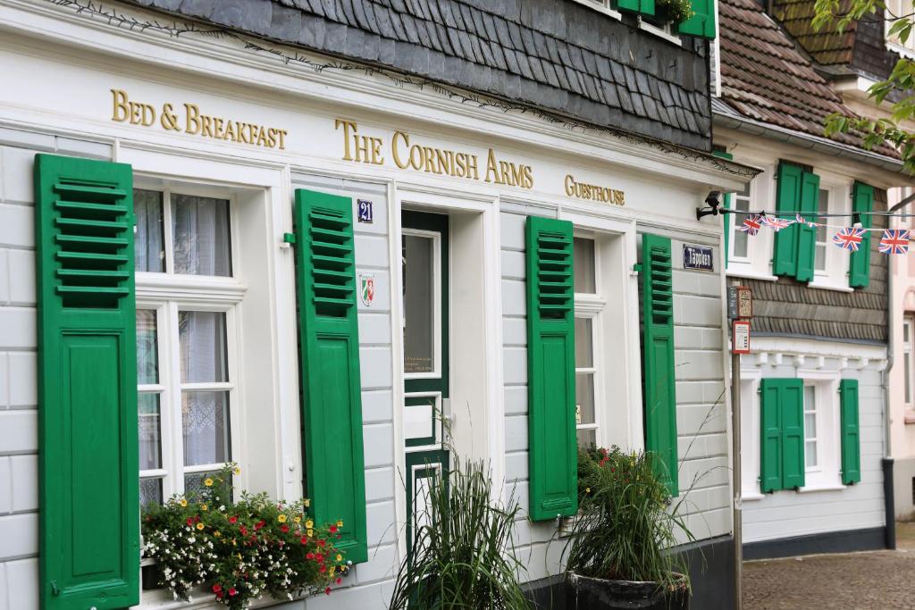 un edificio blanco con flores y ventanas con contraventanas verdes en THE CORNISH ARMS Guest House en Solingen