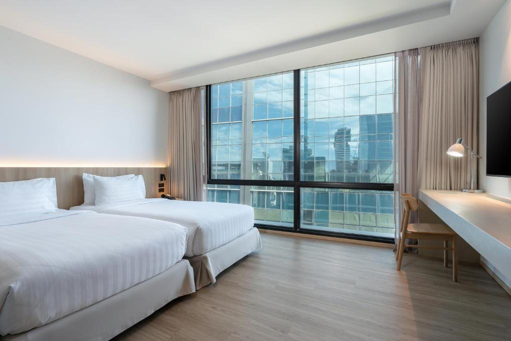 Two beds face a narrow desk and a broad window with a high-rise city view.