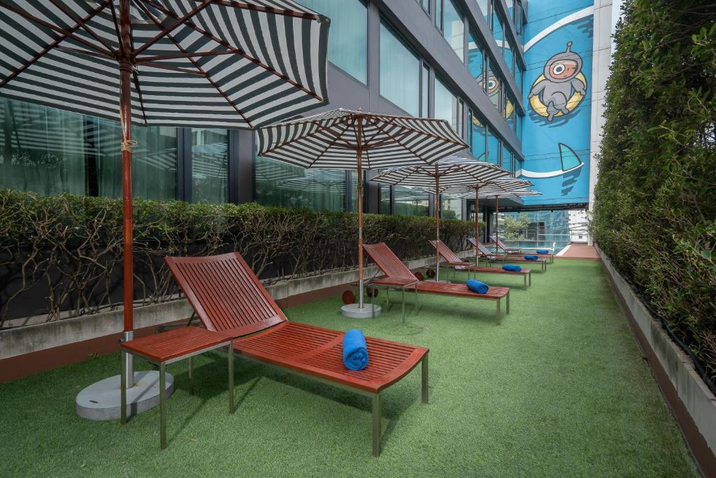 A narrow poolside terrace with striped umbrellas and red loungers.